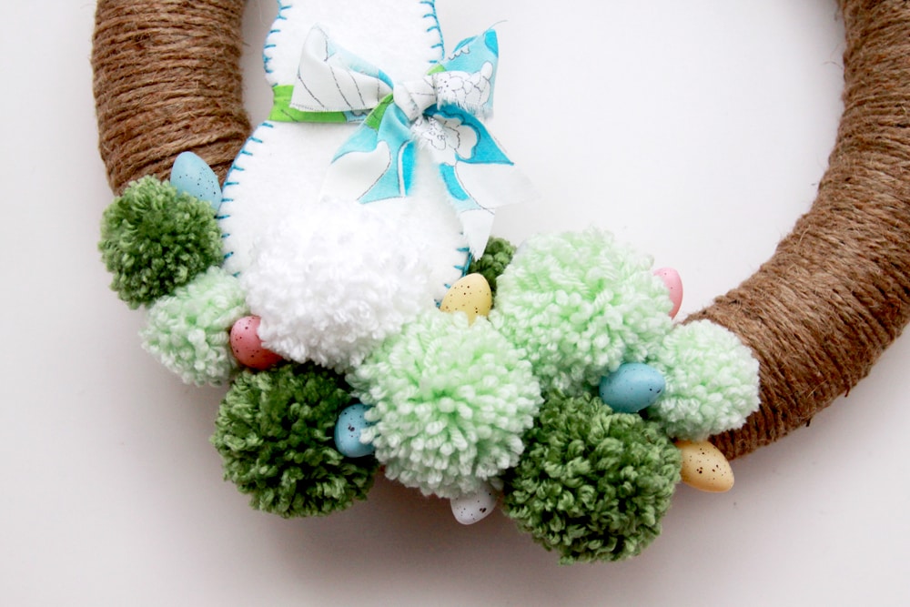 Spring Pom Pom Wreath - so cute! Tutorial on { lilluna.com } Supplies include a foam wreath, fabric, yarn, twine, felt, and mini Easter eggs.