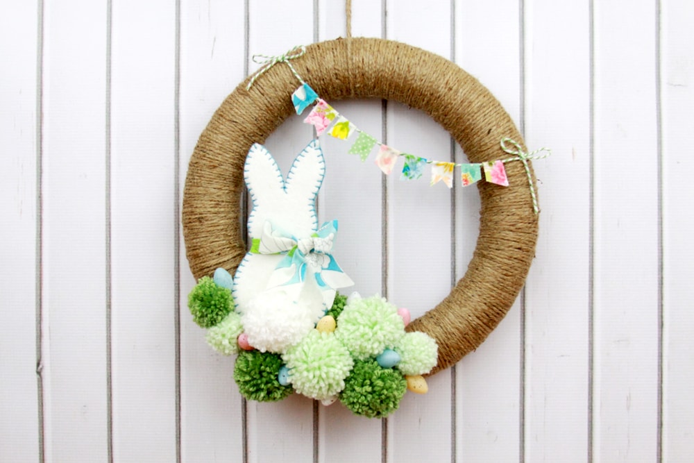 Spring Pom Pom Wreath - so cute! Tutorial on { lilluna.com } Supplies include a foam wreath, fabric, yarn, twine, felt, and mini Easter eggs.