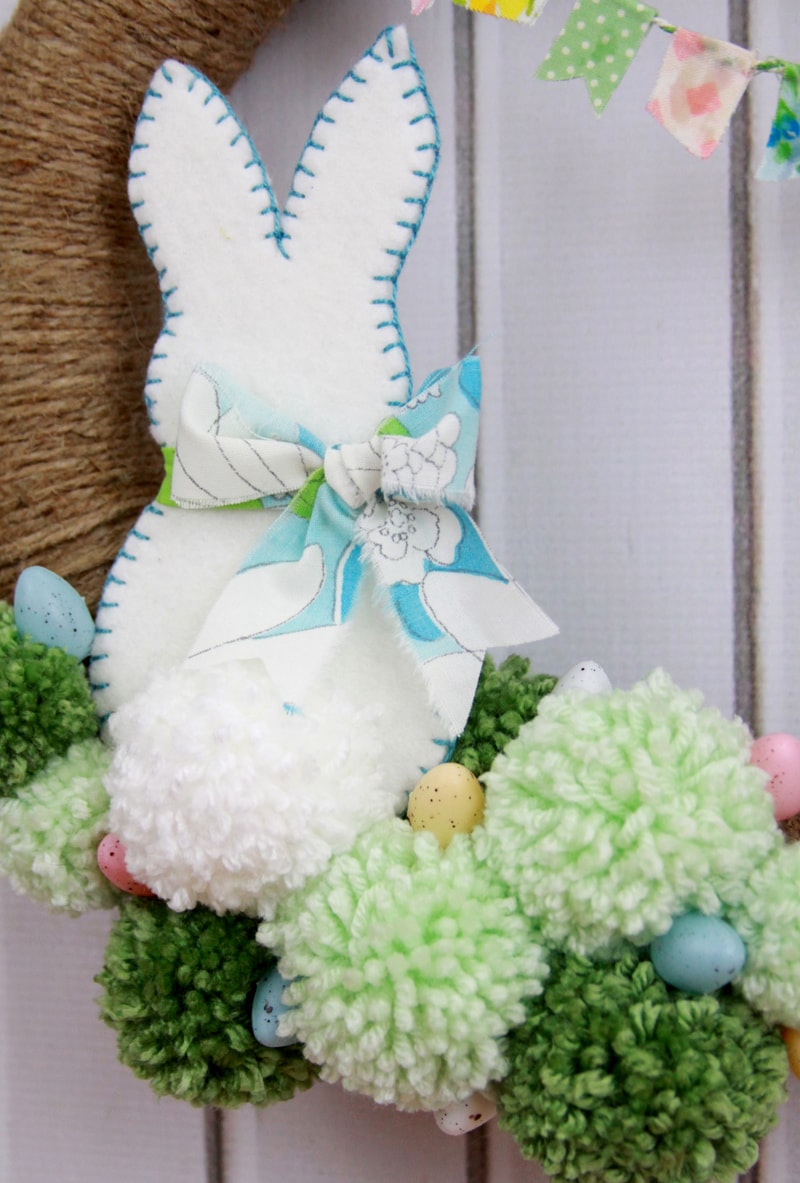 Spring Pom Pom Wreath - so cute! Tutorial on { lilluna.com } Supplies include a foam wreath, fabric, yarn, twine, felt, and mini Easter eggs.