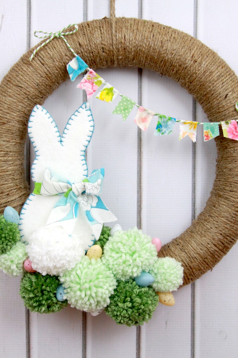 Spring Pom Pom Wreath - so cute! Tutorial on { lilluna.com } Supplies include a foam wreath, fabric, yarn, twine, felt, and mini Easter eggs.