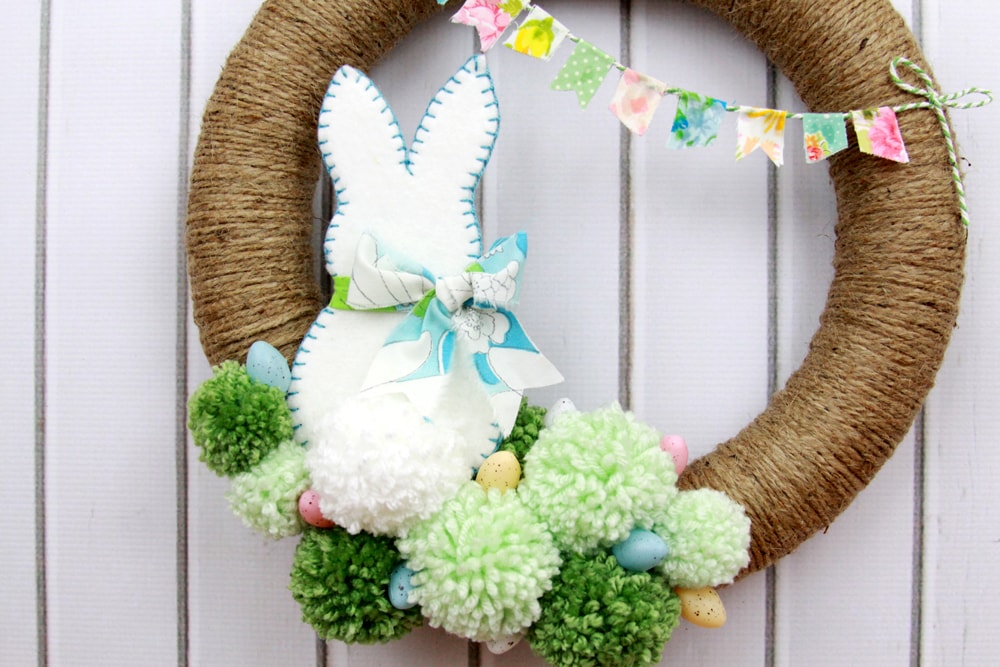 Spring Pom Pom Wreath - so cute! Tutorial on { lilluna.com } Supplies include a foam wreath, fabric, yarn, twine, felt, and mini Easter eggs.