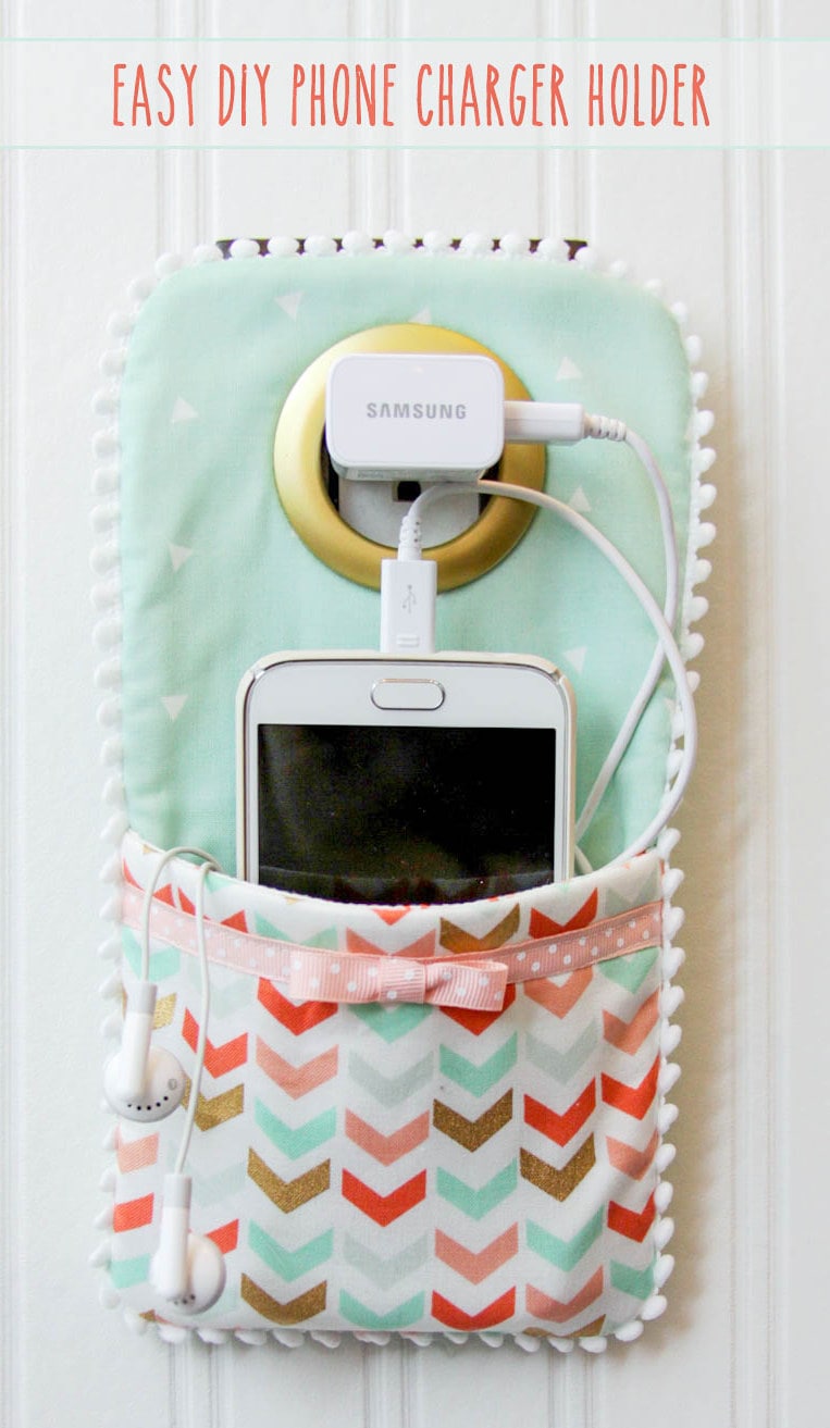 DIY Phone Charger Holder Holder - LOVE this idea!! Supplies needed include - fabric, fusible fleece, ribbon, pom pom trim, and a shower curtain grommet.